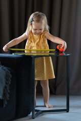 A little two-year-old girl measures the length of the table with a tape measure