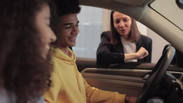 Young couple is sitting inside car and talking to consultant at dealership office spbi. Closeup view of caucasian woman, man sit in auto and look with smiles, talk to seller and make decision to buy