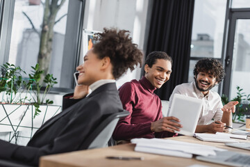 Cheerful multiethnic businessmen using digital tablet while african american colleague talking on smartphone in office.