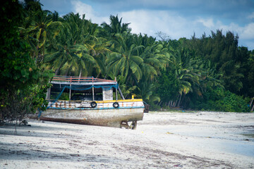 Fishing ship boat stranded on white sand beach with green coconut trees all around and tide coming...