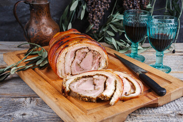 Traditional barbecue Italian porchetta pork belly roll meat as piece and sliced with herbs served...