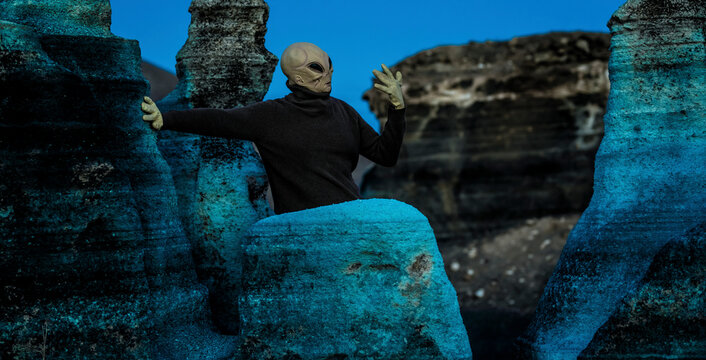 Blue night and alien ufo mask between rocks. Concept of aliens among us. Space discover and future with extraterrestrial life. Horror creepy concept image with monster and scary background