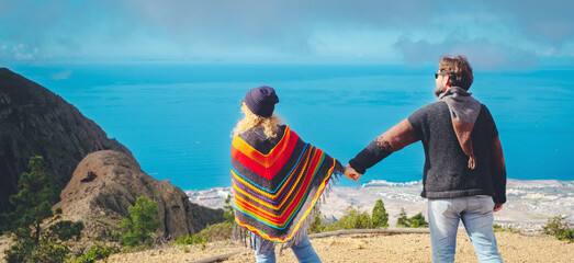 Back view of adult couple holding hands against a beautiful nature bacground with mountains and sea...