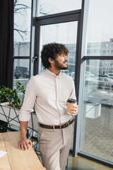 Fototapeta premium Side view of positive indian businessman holding coffee to go in office.