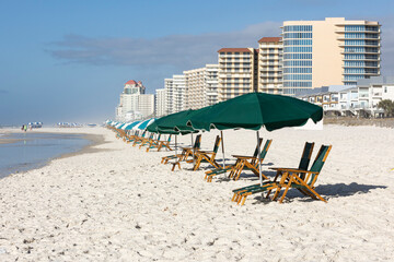 Green beach chairs and umbrellas on a white sand beach with condos in the background on a sunny day.