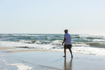 A man in shorts walking along the beach in Orange Beach, Alabama with the Gulf of Mexico waves in the background.