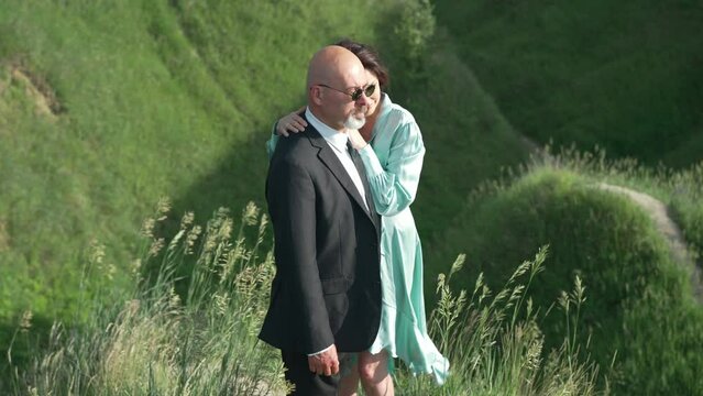 Side view elegant handsome man in suit and sunglasses looking away standing outdoors with beautiful woman in dress. Caucasian husband and wife admiring nature travelling on spring summer day