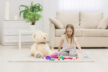 Photo of little girl playing with teddy bear sitting on the floor.