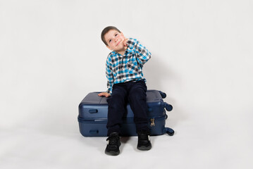 A happy 4-year-old boy sits on a suitcase and smiles, makes a wish, on a white background.