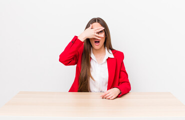 hispanic pretty woman looking shocked, scared or terrified, covering face with hand. business...