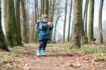 Small kid with photocamera in spring forest. Childhood with nature loving concept