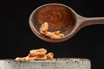 Put caramelized peanuts in salt from a  spoon into a pile on a black background.