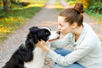 Naklejka na ściany i meble Smiling young attractive woman playing with cute puppy dog border collie on summer outdoor background. Girl holding embracing hugging dog friend. Pet care and animals concept
