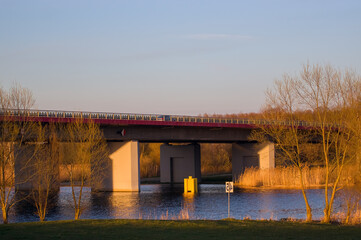 Pięknie oświetlony most nad rzeką w otoczeniu żółtych traw