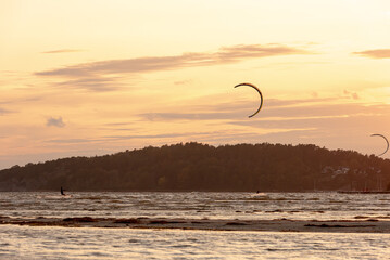 Kiteboarders kitesurfing in the sunset by a beach .