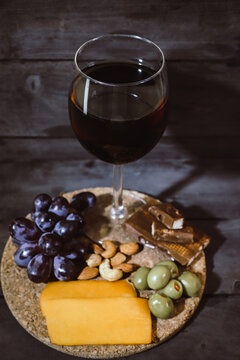 vertical image of glass of red wine with cheese platter with grapes and olives and chocolate and a renaissance style