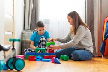 Mother with her son playing with colored cubes sitting on the floor at home. Family spends time together at home in children's room