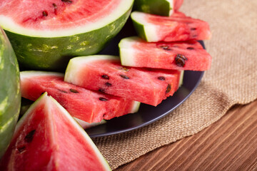 Fresh red watermelon pieces on a black plate on a wooden table. Sweet and juicy watermelon