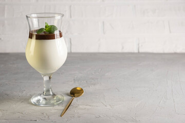 Italian dessert panna cotta served on a white plate with chocolate sauce and fresh mint in glass on a light gray background with copy space