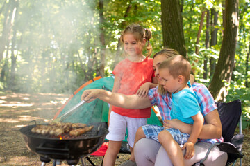 Mother making barbecue with her children in the nature. Family time concept