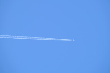 Distant passenger jet plane flying on high altitude on clear blue sky leaving white smoke trace of contrail behind. Air transportation concept
