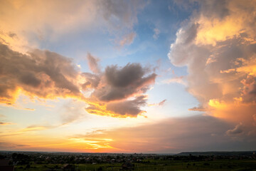 Dramatic sunset landscape with puffy clouds lit by orange setting sun and blue sky.