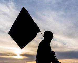 a black silhouette of man with flag on a sunset sky background