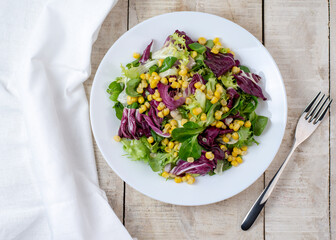 Fresh salad mixed greens (arugula, radicchio, lettuce, corn and radish) on wooden background. Top view. Diet food. Healthy lifestyle