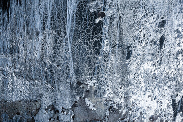 Vertical black rock with ice and snow. Abstraction of an icy rock with snow.