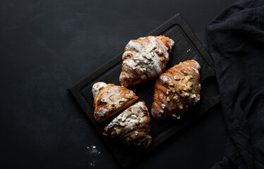 baked croissants on a black wooden board sprinkled with powdered sugar, top view