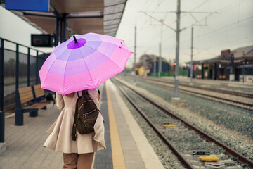Rear view of a woman with backpack and umbrella who waiting train at railway platform.