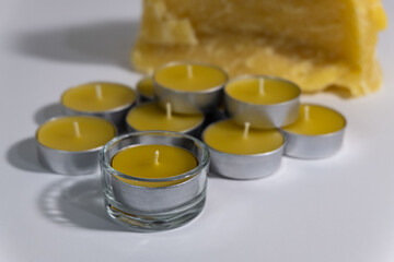 A pile of beeswax tealight candles are displayed with raw beeswax in the background. - obrazy, fototapety, plakaty