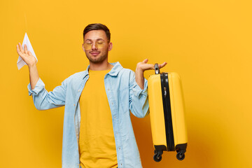 Relaxing happy young tanned handsome man in blue shirt trendy eyewear hold paper airplane suitcase posing isolated on orange yellow studio background. Copy space Banner Mockup. Trip journeys concept