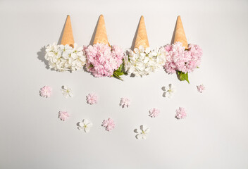 4 Ice cream cone with white and pink spring flowers  over a light background, flat lay. Minimalistic spring design.