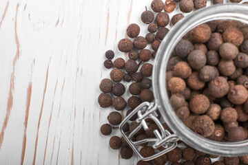 allspice granules in a jar and scattered on a white wooden background top view