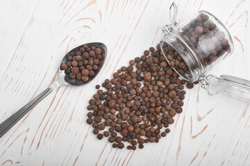 allspice granules in a spoon and scattered from a jar on a white wooden background top view