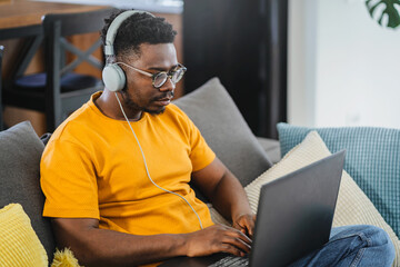 African-American young student man working on a laptop computer at home, listening to online class