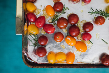 raw whole cherry tomatoes with garlic and rosemary on foil-lined baking tray before roasting