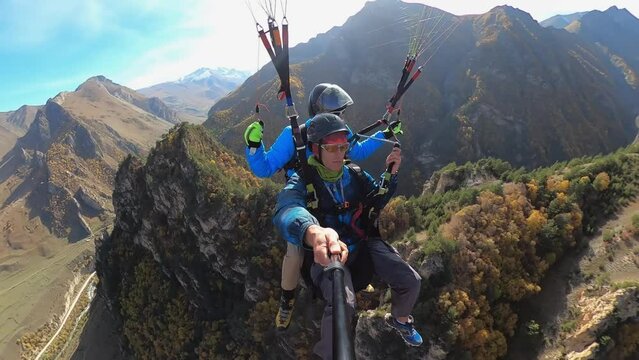 two men fly a paraglider in the highlands, two guys in tandem fly in the mountains, shooting on a monopod gopro