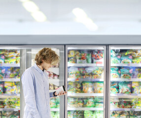  Man choosing frozen food from a supermarket freezer., reading product information