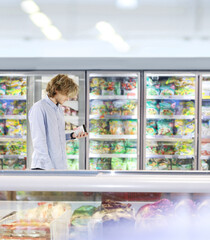  Man choosing frozen food from a supermarket freezer., reading product information