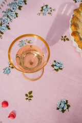 gold rim glass of rose wine on pink tablecloth with blue roses, rhubarb pie on the side