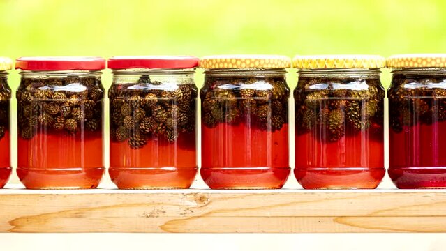 Jam from pine cones in jars.  Spruce jam, footage. Close-up. Glass jars with canning red jam from fir cones on a yellow background. Eco friendly forest products, concept. Canned food. Healthy sweets.