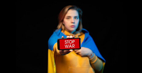 Beautiful Ukrainian girl with a state flag and smartphone in hands with a call STOP WAR. The actual concept of anti-war support. Russian-Ukrainian war. Prays for Ukraine