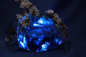 Huge blue  glass stone and apple tree flowers, dark blue spring background, Easter.Huge blue topaz...