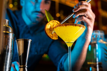 Barman putting a slice of orange in a cocktail in a night club bar