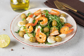 Salad with shrimps, quail eggs, olives and arugula dressed with olive oil and lime juice on a light gray background close-up