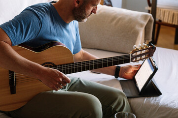 Adult man studying guitar online with tablet at home.