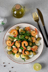Salad with shrimps, quail eggs, olives and arugula on gray background, Top view