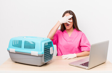 hispanic pretty woman looking shocked, scared or terrified, covering face with hand. veterinarian...